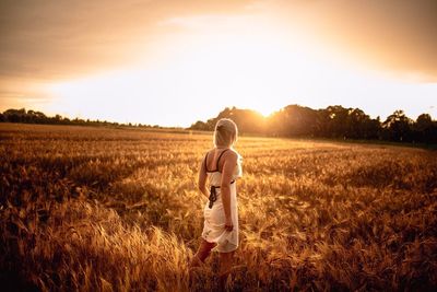 Rear view of man standing on grassy field against sky at sunset