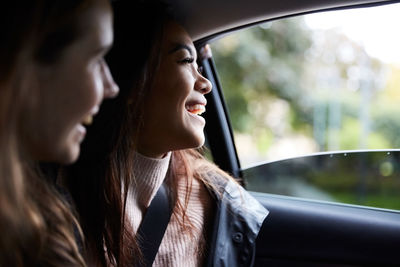 Smiling young female friends looking through window while sitting in taxi