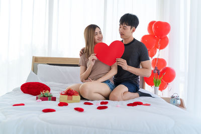 Rear view of two women sitting on bed at home