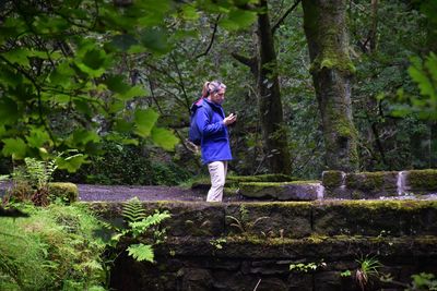 Full length of woman using  her phone standing on bridge in forest