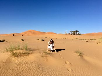 Portrait of woman crouching at desert against clear sky