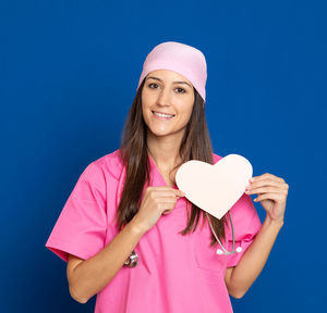 Portrait of a smiling young woman holding pink umbrella against blue sky