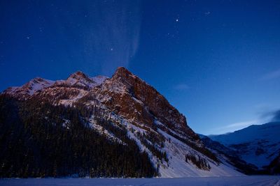 Low angle view of snowcapped mountains against star field at night