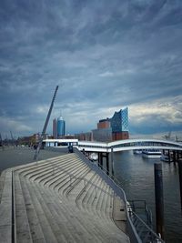 Pier over river by buildings in city against sky