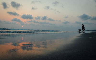 People on beach against sky during sunset