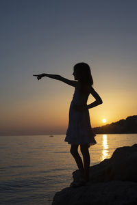 Silhouette woman standing at beach during sunset