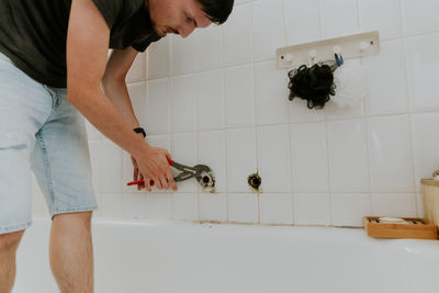 A young man unwinds the faucet tube in the bathroom.