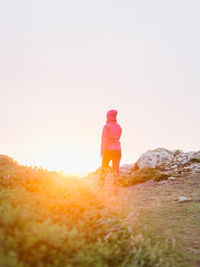 Rear view of man standing on field against sky during sunset