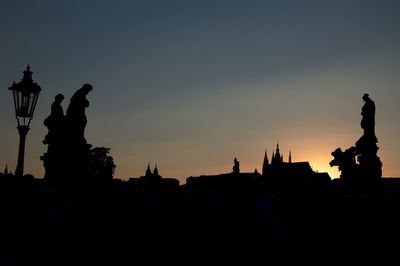 Silhouette of statue in city at sunset