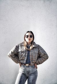 Portrait of young woman wearing sunglasses while standing against wall