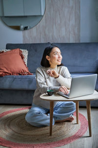 Young woman using laptop while sitting on sofa at home