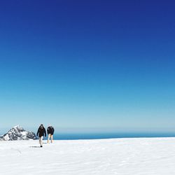 People on sea shore against clear blue sky