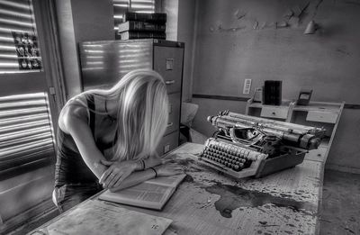 Woman with book by typewriter on table at office