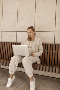 Woman using laptop while sitting on bench