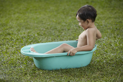 Shirtless boy sitting in bathtub on field at yard