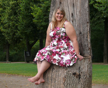 Portrait of smiling woman sitting on tree stump