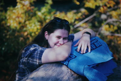 Portrait of young woman leaning on tree stump in forest