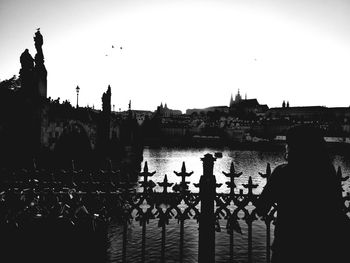 Silhouette people by river in city against clear sky