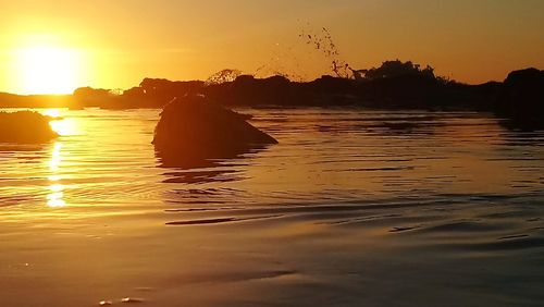 Silhouette rocks in sea against sky during sunset