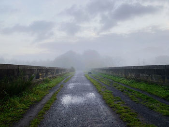 Misty road amidst field against sky