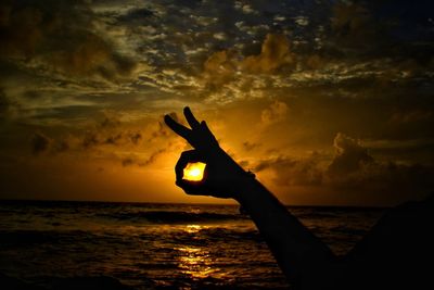 Silhouette hand on sea against sky during sunset