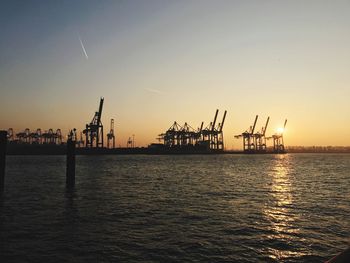 Cranes at commercial dock against sky during sunset