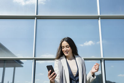 Young woman using phone while standing on window