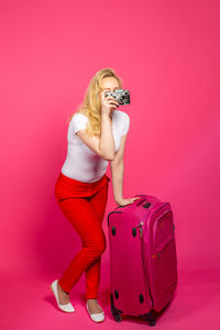 Young woman holding umbrella against pink background