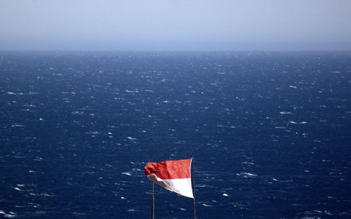 Waving flag by sea against sky