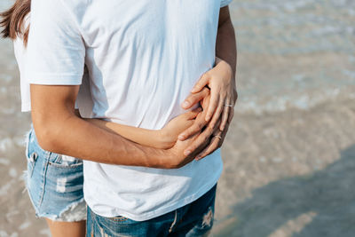 Midsection of woman embracing partner at beach