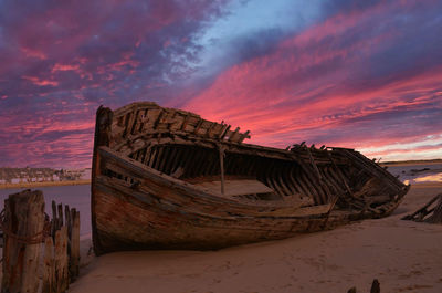 Abandoned boat on beach against sky during sunset