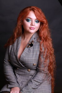 Portrait of sensuous young woman wearing gray blazer while sitting against black background