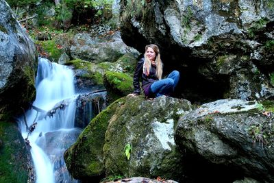 Young woman sitting on rock by waterfall