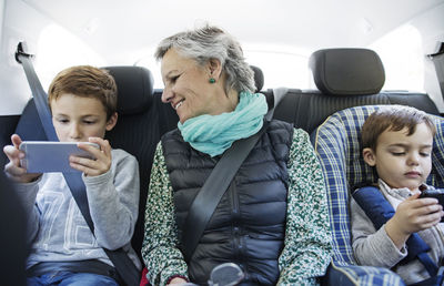 Senior woman looking at grandson using smart phone in car