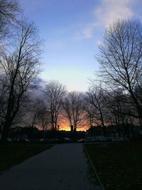 Bare trees by road against sky during sunset