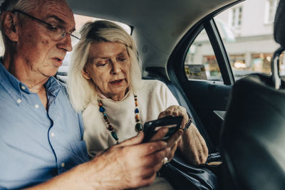 Senior couple using smart phone while sitting in taxi