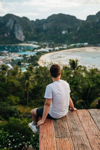 Rear view of man sitting on wood over trees