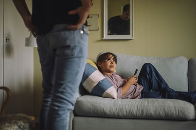 Girl with smart phone looking at father standing near sofa at home