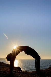 Silhouette of woman with nice body performing inverted yoga pose at sunrise. vertical format