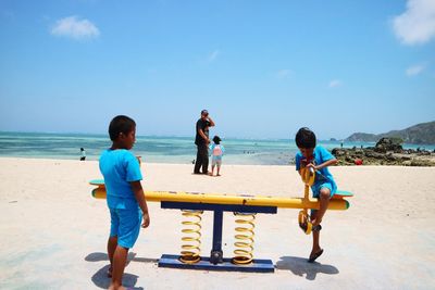 Boys playing on seesaw at shore of beach