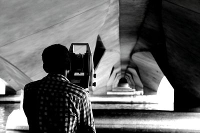 Rear view of man with theodolite under bridge