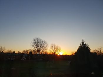 Silhouette trees on field against clear sky during sunset