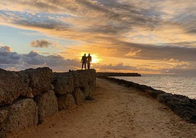 Men standing on beach against sky during sunset