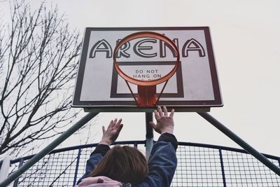 Low angle view of woman reaching basketball hoop against sky