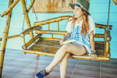 Woman holding book while sitting on swing