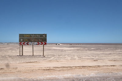 Information sign on beach against clear blue sky