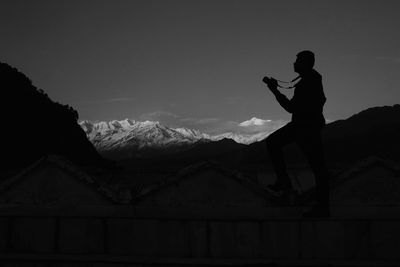 Silhouette man standing with camera on mountain against sky