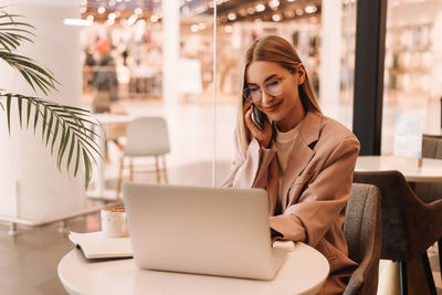 A millennial business woman with glasses works and studies using mobile phone and technology in cafe