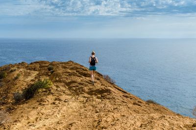 Rear view of woman walking on rock by sea against sky