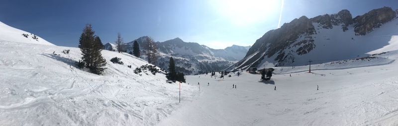 Panoramic view of people skiing on snowcapped mountain against sky